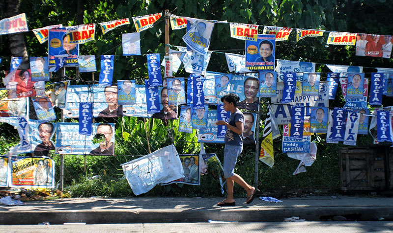 A passerby ignores the campaign posters of both local and national candidates that practically cover this side of Davao City’s Buhangin District. (davaotoday.com photo by Wether b. Saldaña)