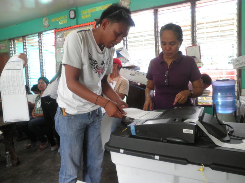 TRY & TRY.  A voter in Panabo City attempts to feed the ballot to the PCOS machine five times, to no avail.  (davaotoday.com photo by Mart D. Sambalud) 