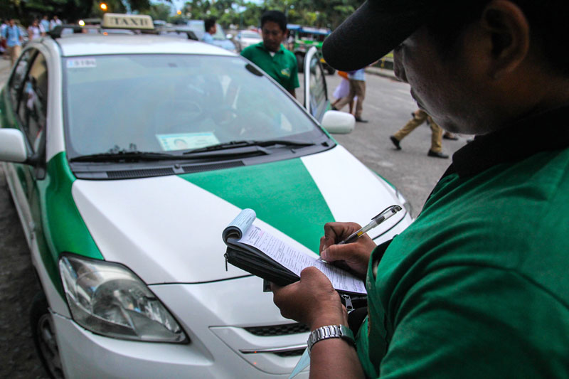 ALARM.  A traffic enforcer in Davao City issues a violation ticket against a cab driver for illegal terminal, when he parked his vehicle outside the school along Roxas Street.  (davaotoday.com photo by Ace R. Morandante)