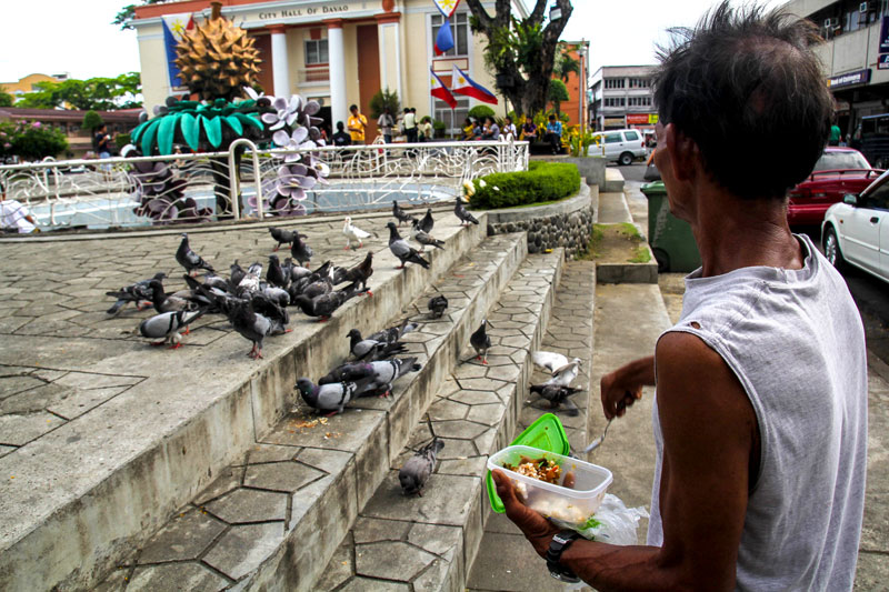 SHARING IS LOVING.  A shoe repair man shares his modest lunch with the doves outside the Davao City Hall building.  (davaotoday.com photo by Ace R. Morandante)