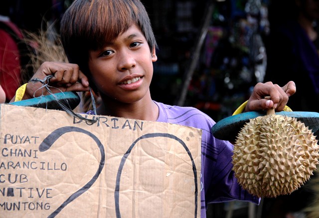 HANDS FULL A boy at Bankerohan Public Market tries holds a durian in one hand and a price tag in another hand as he enticed market-goers.  Despite of the low price, durian and other market products however are earning less due to the security issues hitting the city. (davaotoday.com photo by Medel V. Hernani)