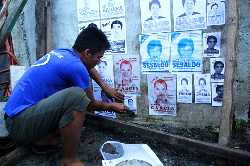 A man volunteers in pasting mini-posters for a candidate in the October 28 Barangay Election. (davaotoday.com photo by Ace R. Morandante)