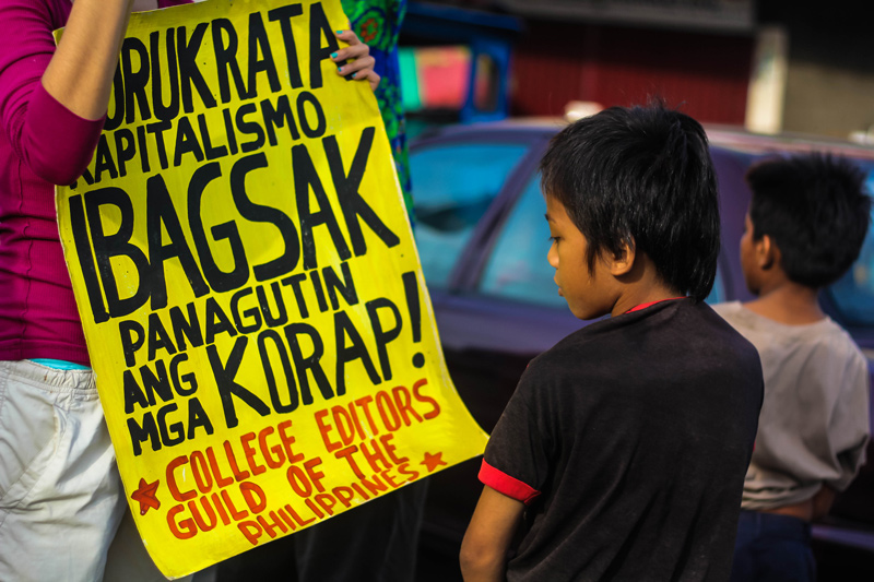 READING THE SIGNS A kid reads a protester's placard slamming 'bureaucrat capitalism' or the abuse of government  position for personal gain, during Wednesday's protest by Youth Act Now, which condemned the retention of Presidential pork barrel known as Presidential Social Fund and the Disbursement Acceleration Program (DAP). (davaotoday.com photo by Ace R. Morandante)