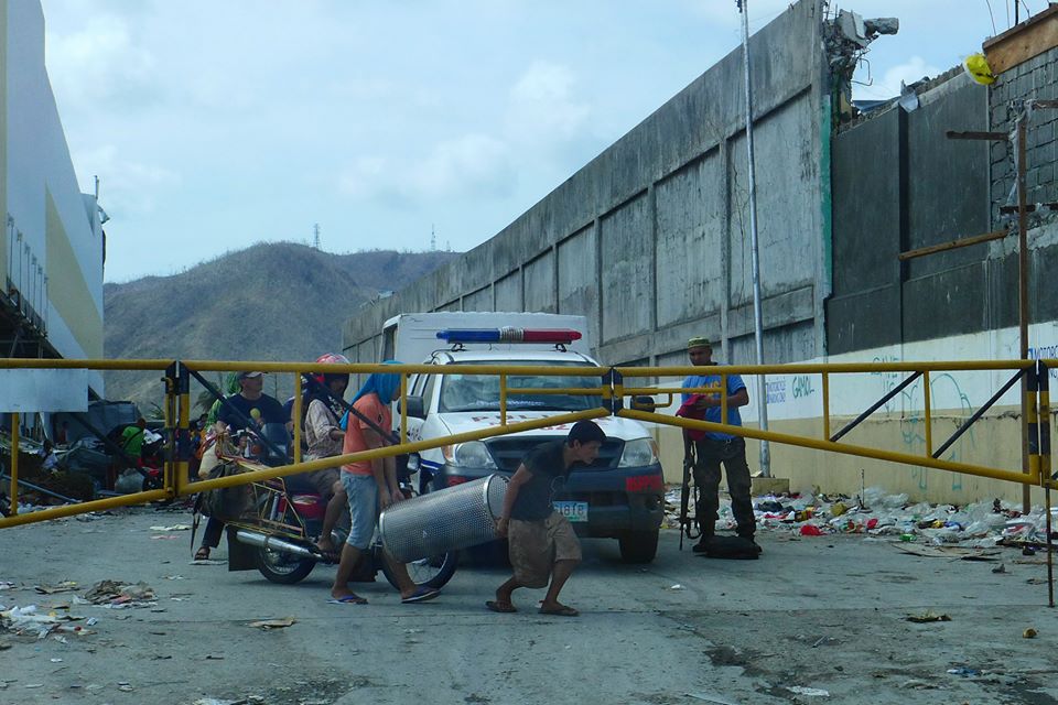 IN PLAIN SIGHT This contributed photo from Tacloban City shows people carting off goods from Robinson's Mall last Monday in plain sight of an armed security guard who could only watch . Chaos and hunger has stricken this city struck by Typhoon Yolanda last Friday, as no clear system has been implemented to carry off the dead and take care of the many survivors. (Contributed photo by Arthur Yap)