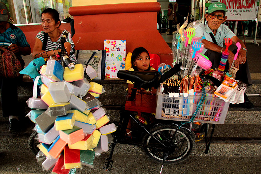 A girl guards her father's bike full of assorted products to sell around downtown. (Ace R. Morandante/davaotoday.com)