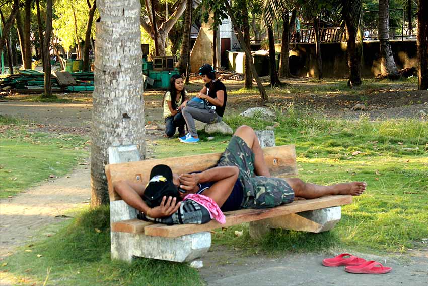 A man busies himself with his mobile phone, while a couple takes photographs of each other at Magsaysay Park. (Medel V. Hernani/davaotoday.com)