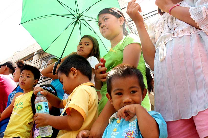 Mothers and their children bear the hot weather while watching the civic parade. (Medel V. Hernani/davaotoday.com)
