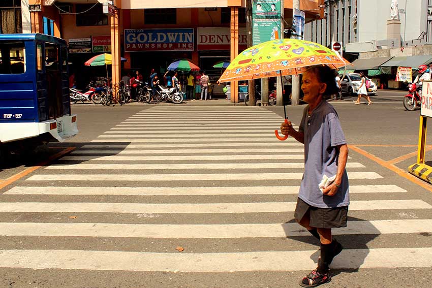 An elderly woman crosses a downtown street in Davao City wearing socks and an umbrella to protect her from the El Nino heat. As many as 11,000 farmers are expected to be affected by the dry spell. (Medel V. Hernani/davaotoday.com)