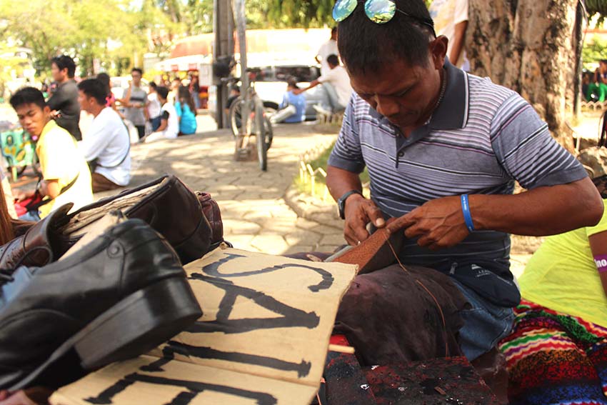 A mobile shoe repair man rushes the repair of sandals and shoes for display at Rizal Park. He is anticipating an increase in needs on graduation day. (Medel V. Hernani/davaotoday.com)