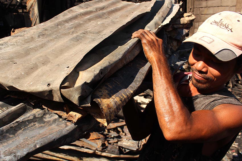 A man carries a bundle of charred GI sheet from the fire victims' house: in the area. 57 houses in Barangay Bucana were ravaged by fire on Wednesday night.