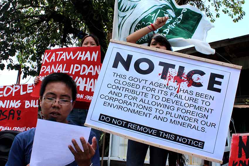 Prof. Kim Gargar of the environmental organization Panalipdan unfolds the content of the closure notice in front of the office of XI Regional Director of Mines and Geoscience Bureau at A. Quezon Street, Davao City.