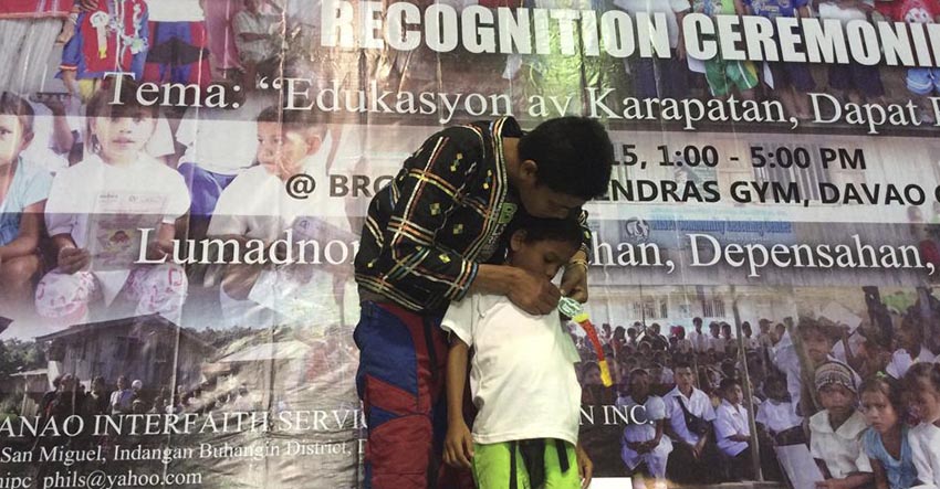 Crispin Subla pins the ribbons to son, Miguel who will be entering Grade 1 this school year during the moving-up ceremony of Misfi Academy held here on Monday. 52 students had to travel for several hours just to attend their recognition rites allegedly because a paramilitary group refuses the school's operation. (Photo contributed by Glades Jane Maglunsod)