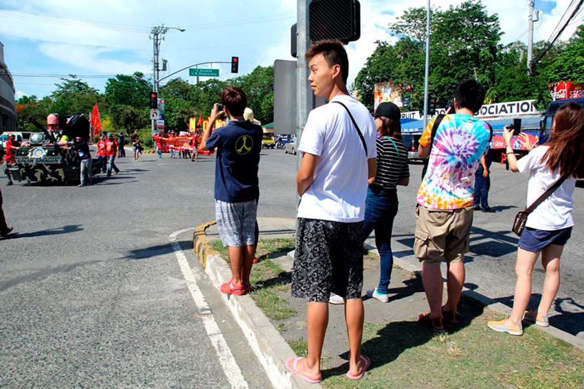 Korean tourists take photographs of protesters while they march during the celebration of the 129th International labor Day. (Ace R. Morandante/davaotoday.com)