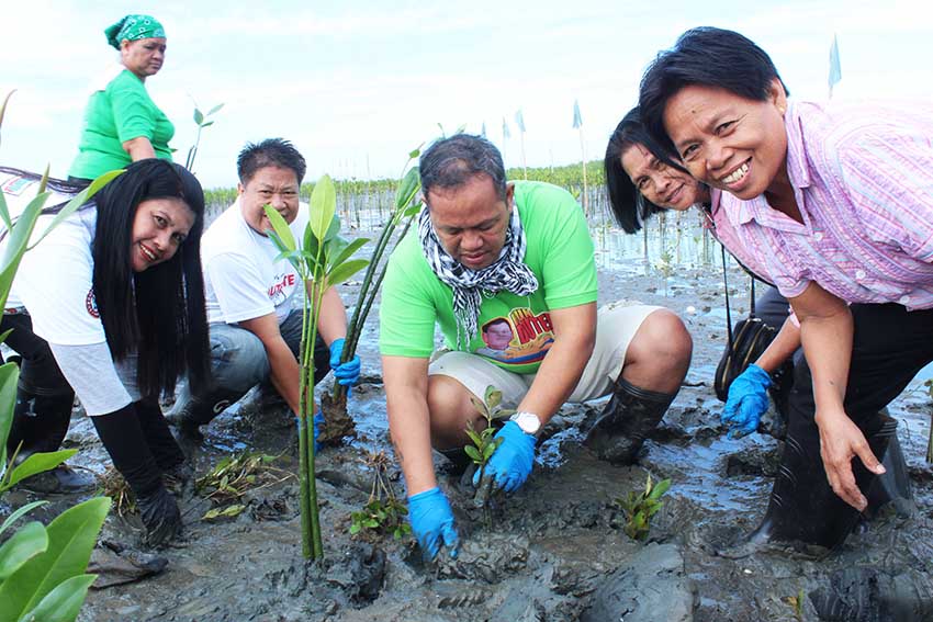 Participants of the tree planting  organized by the City Environment and Natural Resources Office (Cenro) early morning Saturday in Barangay 26-D, Davao City pose for the camera while planting mangrove seedlings. They say the mangroves will protect the community from huge sea waves. (Medel V. Hernani/davaotoday.com)