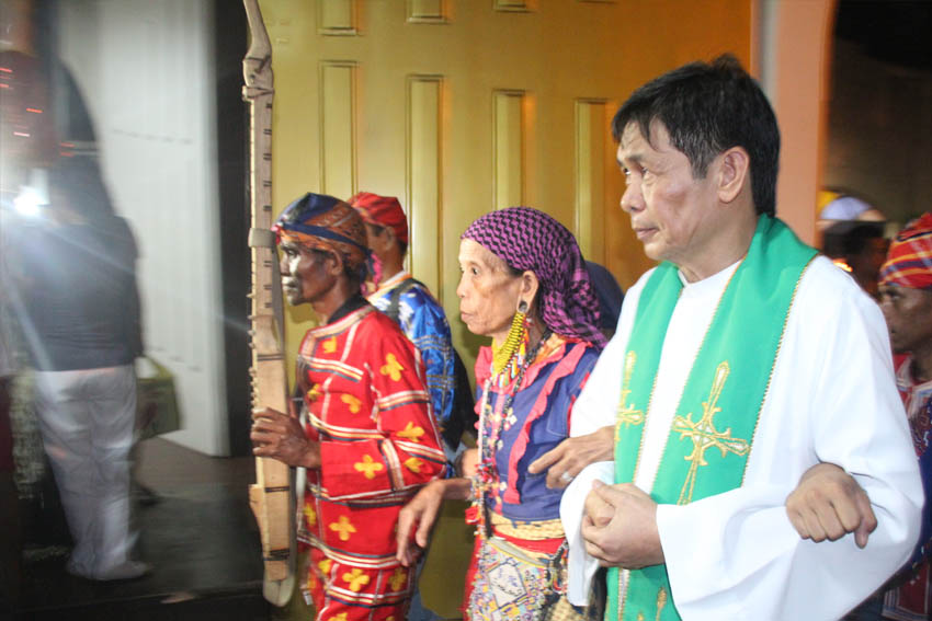 INTERFAITH.​ Father Teody Holgado, head priest of Baclaran church, links arms with Mindanao's first woman chieftain (center) along with other Lumad leaders in Pasay City, Sunday evening. The Lumads are in Manila to campaign against Lumad killings and to call for the pull out of military troops from their communities. (Earl O. Condeza/davaotoday.com)