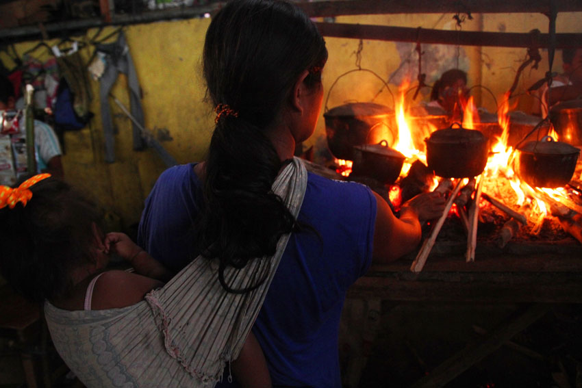A Lumad woman carries her daughter while cooking early in the Buhangin gym where hundreds of IPs are currently staying. (Ace R. Morandante/davaotoday.com)