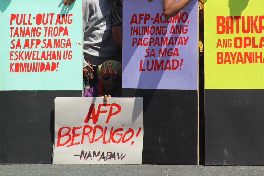 A protester takes a quick respite from the heat as he snuggles under the placards during their blockade in front of the Eastern Mindanao Command camp. 