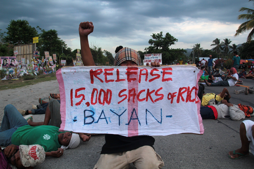 RAISED FIST. An activist raises his fist while holding a streamer with the demand for 15,000 sacks of rice. Behind him are farmers sprawled in the national highway of Koronadal-Gen.San. (Ace R. Morandante/davaotoday.com)