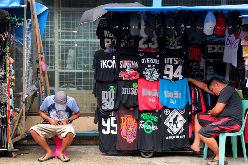 AFTERNOON SCENE. A printed shirt vendor snatches a nap while waiting for customers. A man nearby makes a fancy necklace, Friday afternoon in San Pedro street. (Ace R. Morandante/davaotoday.com)