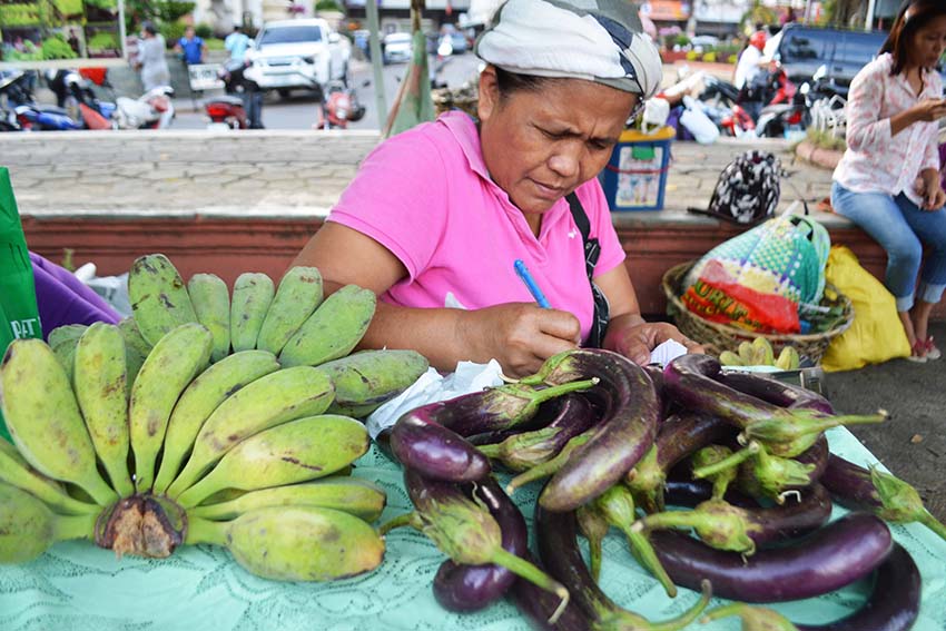 A woman farmer from Barangay Waan, Buhangin District, Davao City, computes her sales for selling vegetables and banana in Rizal Park here  Friday, Oct. 14. (Medel V. Hernani/davaotoday.com)
