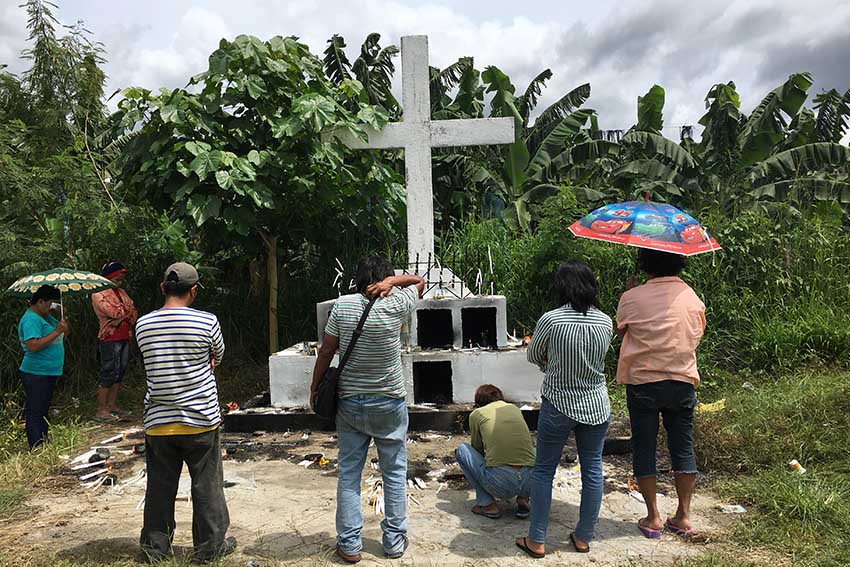 A number of people offer prayers for the souls of their departed loved ones before a life-size white cross inside the Davao Penal and Prison Farm Colony cemetery at Braulio Dujali, Davao del Norte during the annual observance of “Undas.” (Mart D. Sambalud/davaotoday.com)