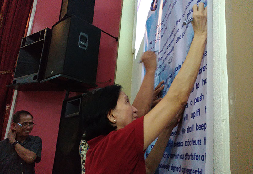 National Democratic Front of the Philippines peace consultant Wilma Tiamzon signs the unity statement for peace during the peace forum and assembly held at the University of the Immaculate Conception in Davao City on Saturday afternoon, Dec. 3. Behind her is husband, Benito Tiamzon, NDF peace panel member. (Zea Io Ming C. Capistrano/davaotoday.com)